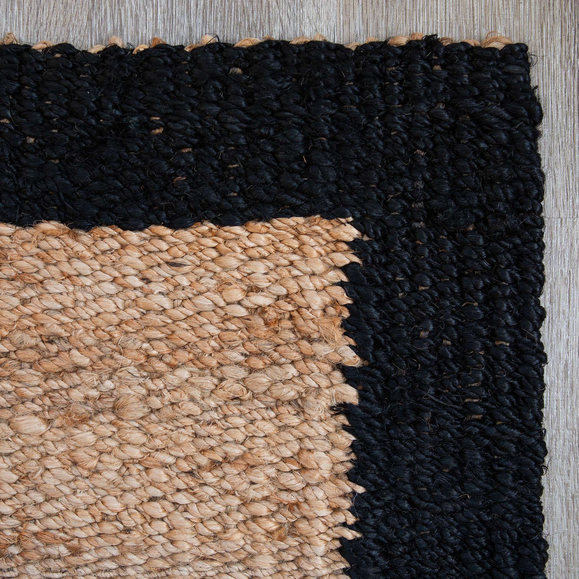 Close-up view of a woven-border jute mat, natural in colour with a blackcolour border.