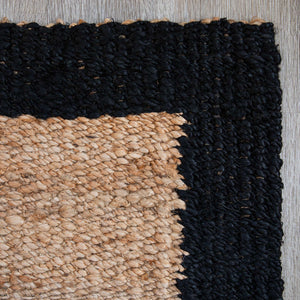 Close-up view of a woven-border jute mat, natural in colour with a blackcolour border.